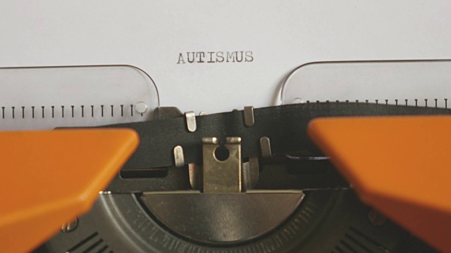 一个人用声音在一台旧打字机上写AUTISMUS的特写镜头视频素材