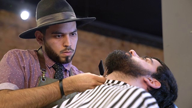 年轻的理发师在沙龙为顾客修剪胡须视频素材