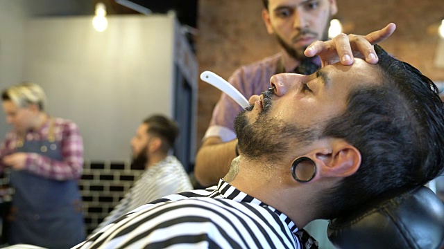 年轻的理发师用直刮胡刀刮胡子视频素材