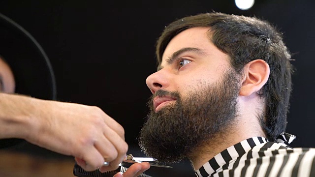 理发师在沙龙为年轻的顾客修剪胡须视频素材