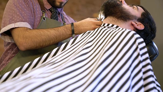 年轻的理发师在沙龙为顾客修剪胡须视频素材
