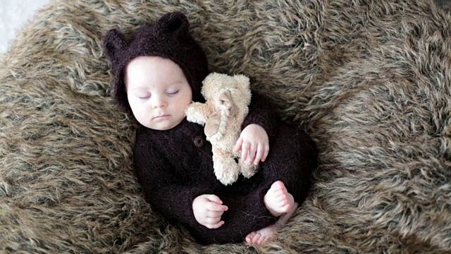 小男孩穿着编织成棕色的连衣裤像一只小熊，睡在家里毛茸茸的毯子上，开心地笑着视频下载