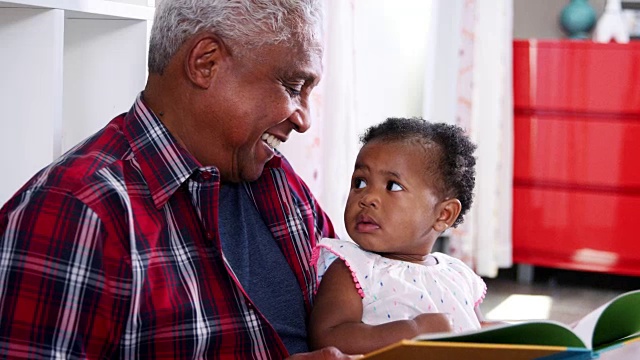 爷爷和小孙女坐在家里一起看书——慢镜头视频素材