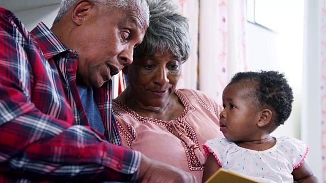 爷爷奶奶和小孙女坐在家里一起看书——慢镜头视频素材