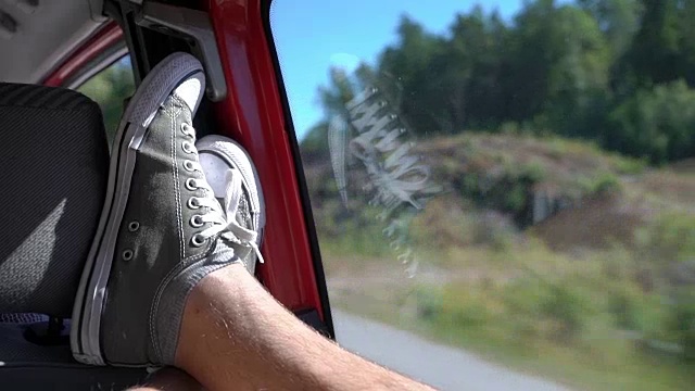 一个喜欢开车旅行的年轻人把她的腿扔在窗户上。视频素材