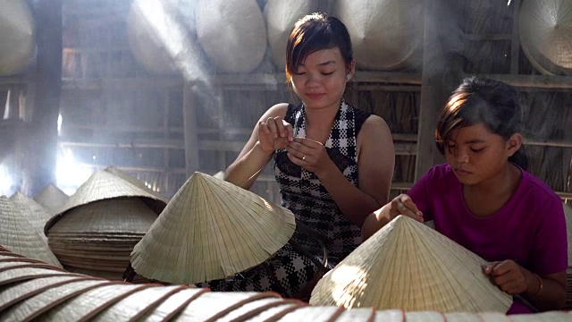 两名同胞越南工匠在老传统房子制作传统越南帽子的4k镜头低光场景，在Ap Thoi Phuoc村，Cantho省，越南，传统艺术家的概念视频下载