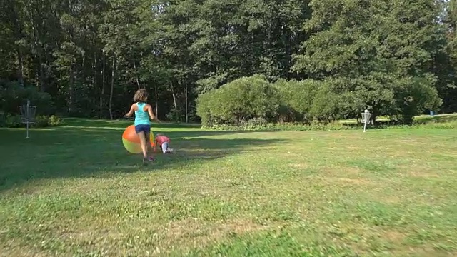 两个不同年龄的可爱女孩玩着一个巨大的彩色彩虹充气球。视频素材