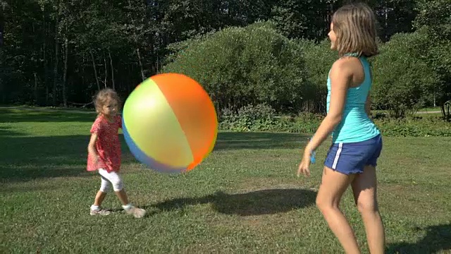 两个不同年龄的可爱女孩玩着一个巨大的彩色彩虹充气球。视频素材