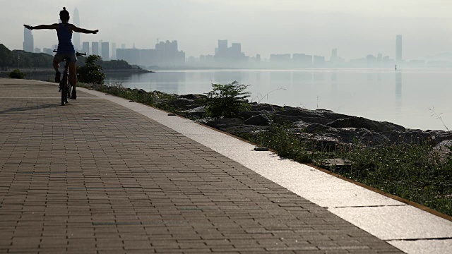 日出时分，一个女人在海边的路上骑着自行车，双手举在空中视频素材
