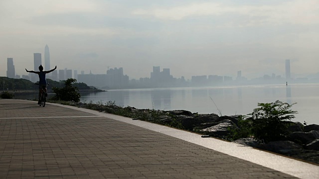 日出时分，一个女人在海边的路上骑着自行车，双手举在空中视频素材