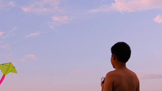 小男孩在日落时在海滩上玩风筝，慢镜头。视频素材