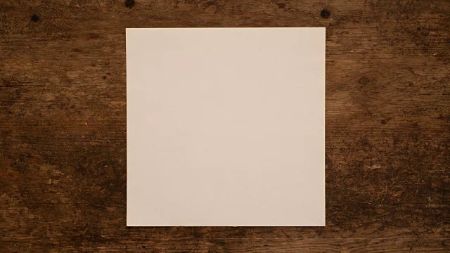 在木质背景上打开和包装一张正方形的纸。在木板上折叠和展开方形空白纸。视频下载