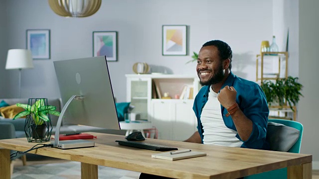快乐的年轻人在家里使用个人电脑，赢大钱，打空气拳，情绪上庆祝胜利。在舒适的客厅背景。视频素材