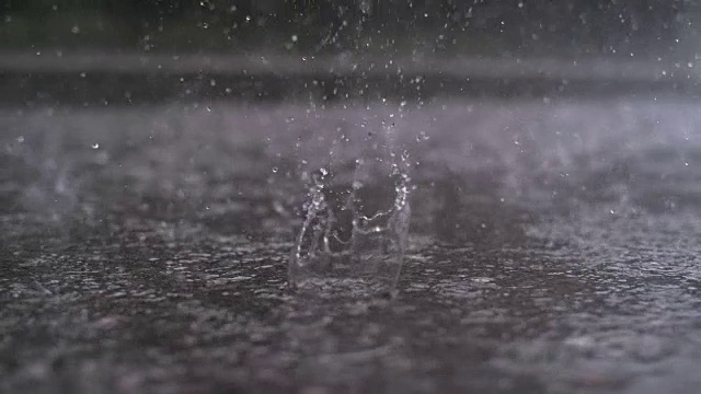 慢镜头特写:雨滴落在街道上，形成一个大水坑视频下载