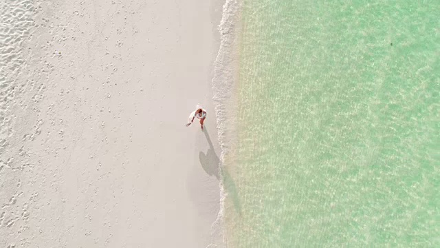 MS to WS Woman走在阳光明媚的马尔代夫田园般的热带海滩上视频素材