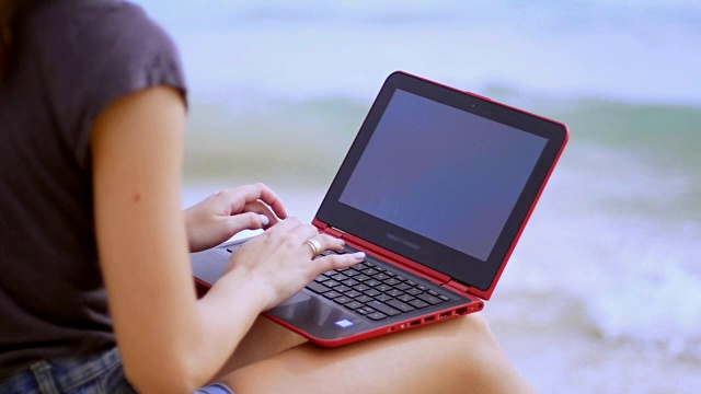 用笔记本电脑工作的女孩。在沙滩上用笔记本电脑打字视频素材