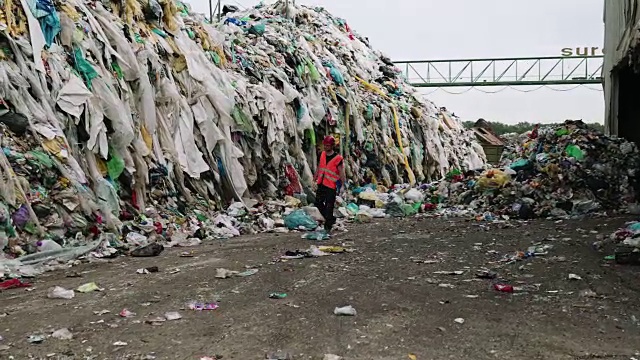 工人走过垃圾处理场的巨大垃圾堆视频素材