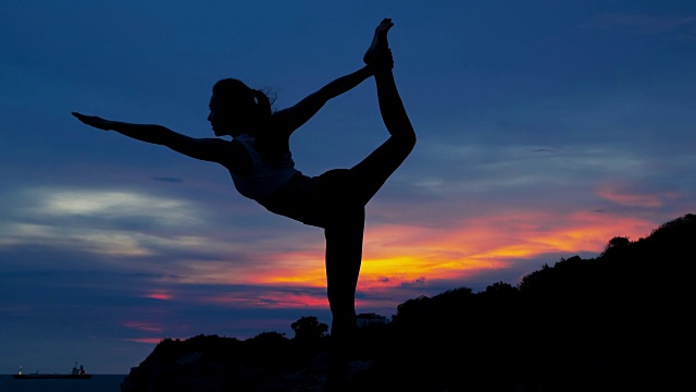 剪影一个年轻女子在山海练习瑜伽。视频下载