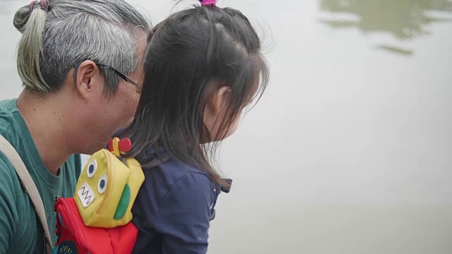亚洲年轻的母亲和年轻的父亲和她可爱的两岁的女儿在户外玩耍，用食物喂鱼和乌龟。家庭观念，爱自然。幸福的孩子有父母的爱。视频素材