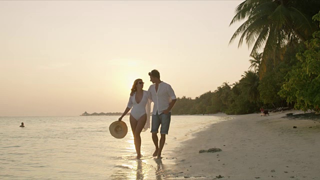 马尔代夫，一对宁静的夫妇手牵着手，在日落时分漫步在宁静的热带海滩上视频素材