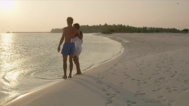 马尔代夫，一对深情的情侣站在日落时分宁静的热带海滩的水边视频素材