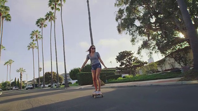 迷人的冒险女孩滑板下的棕榈树排列的街道在日落视频素材