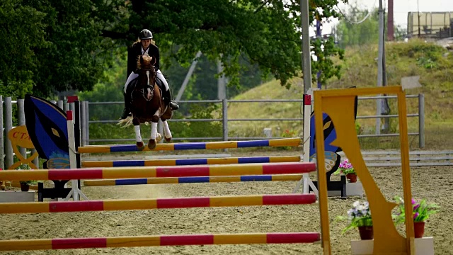 慢镜头:一名身穿黑白制服的女骑师骑在马上跳过障碍。马术比赛。视频下载