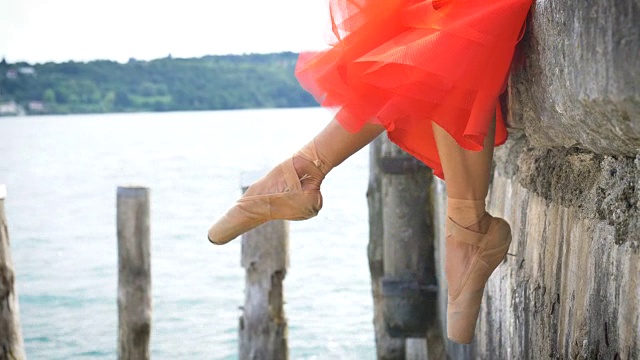 一个美丽的芭蕾舞女演员在白色的裙子，而她是挂她的脚在湖上的特写视频素材