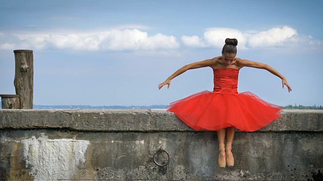 一个美丽的轻芭蕾舞女演员的肖像，在一个茂盛的红色连衣裙，而她正在跳舞。视频素材