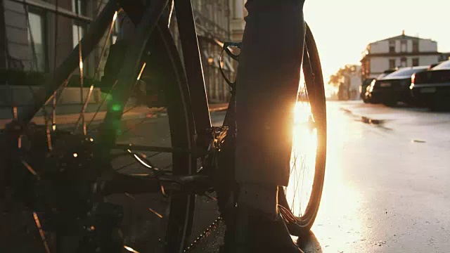 近距离拍摄的英俊的年轻人驾驶他的自行车在街道上的城市中心在日出，慢动作视频下载