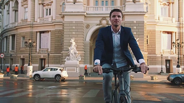 英俊的年轻人驾驶着他的自行车在城市中心的街道上的建筑背景，慢镜头视频素材