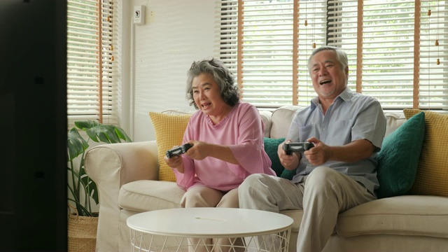 亚洲老年夫妇在家里一起玩游戏，心情愉快。人们以放松、养老、退休、高级生活方式为家庭观念。视频素材