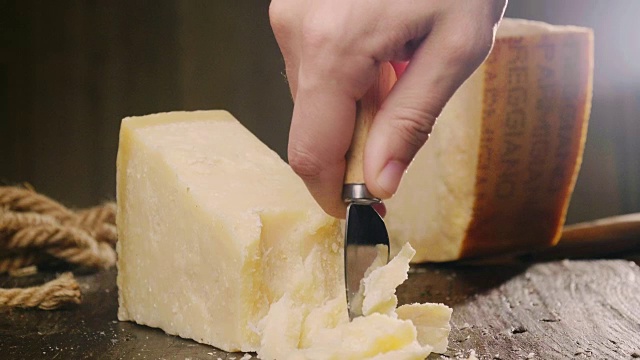 帕尔玛干酪的混合物，放在木砧板上。一只手拿着刀，掰开几块来品尝质量。视频下载