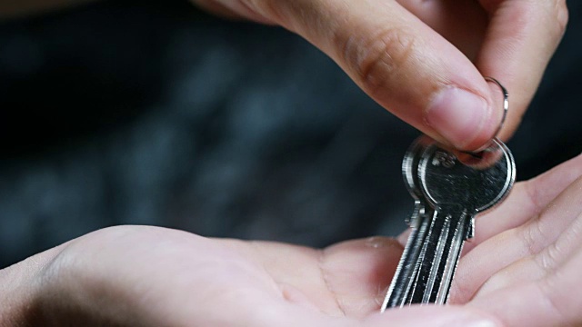 房子的钥匙或另一把锁，把钥匙放在他手里，放在一个黑暗的背景上。视频下载