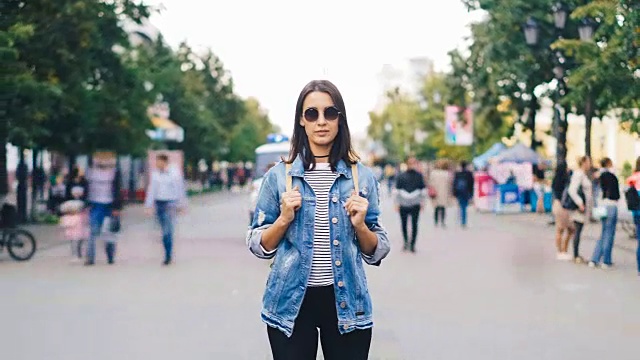 在繁忙的步行街人流中，一位自信的年轻女士戴着太阳镜看着镜头，将镜头拉近。青年与社会观念。视频素材