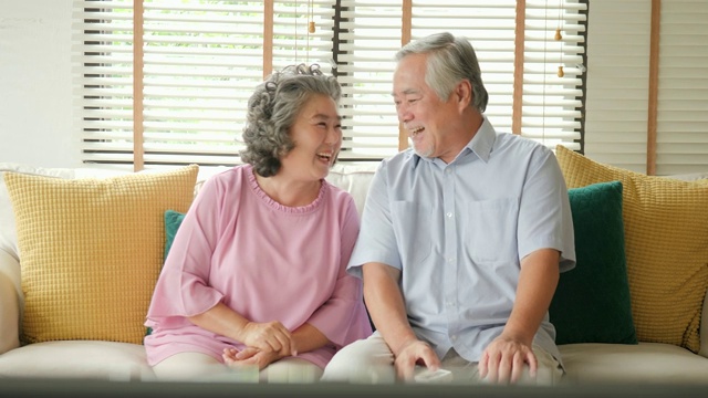 快乐的老两口一起看电视。人们以放松、养老、退休、高级生活方式为家庭观念。视频素材