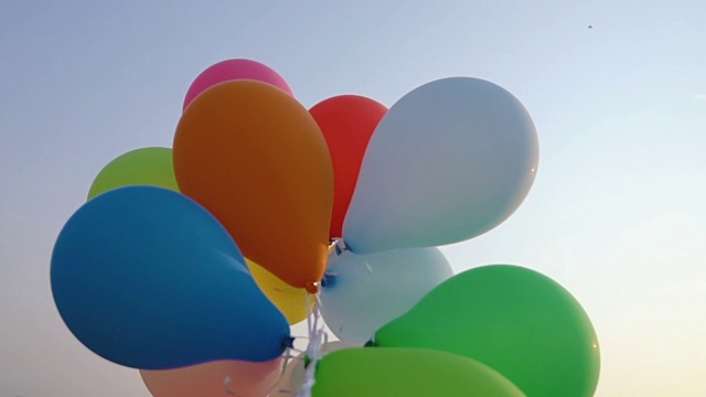 在夏日的蓝天下，手握一串五颜六色的气球视频下载