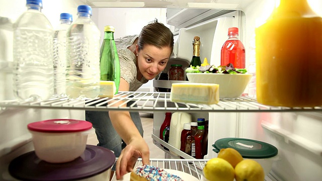 女人打开冰箱，咬了一口甜甜圈视频素材