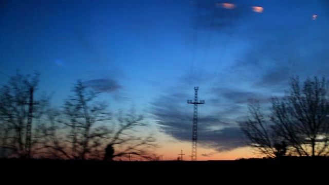 日落时路过的风景乘客POV，梦幻的风景。道路上树木和电线的剪影视频素材