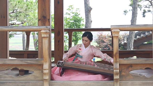 一名女音乐家穿着韩服(韩国传统服装)在凉亭中弹奏伽倻琴(有12根弦的韩国古筝)视频素材