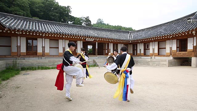 四物乐(起源于韩国的一种打击乐)的团队在一个韩国风格的房子的院子里演奏乐器视频素材