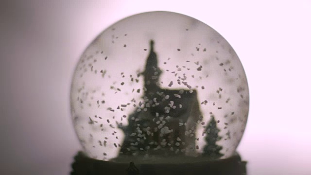 近距离拍摄的“雪”在一个塑料教堂周围旋转，然后落在一个雪球的底部。视频下载