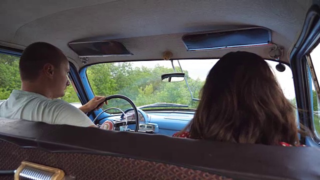 年轻夫妇骑着老爷车，戴着帽子。不认识的男人和女人坐在前座的旧复古汽车在公路旅行。旅行的概念。慢镜头后视图视频素材