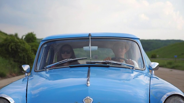 年轻夫妇戴着帽子，开着老爷车在夏天旅行。男人和女人坐在老爷车的前座期间。假日公路旅行的概念。慢动作近距离前视图视频素材