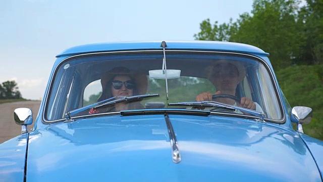 年轻夫妇戴着帽子，开着老爷车在夏天旅行。男人和女人坐在旧复古车的前座，在行驶中交谈。假日公路旅行的概念。慢镜头视频素材