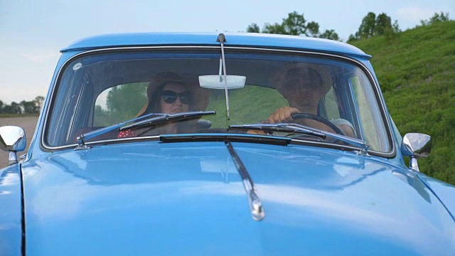 年轻夫妇戴着帽子，开着老爷车在夏天旅行。男人和女人坐在旧复古车的前座，在行驶中交谈。假日公路旅行的概念。慢镜头视频素材