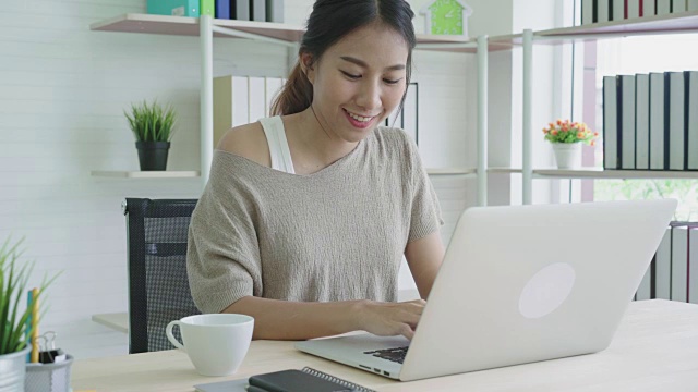 迷人的年轻亚洲女人微笑积极和喝咖啡休息感觉放松和平静的家庭办公室。视频素材