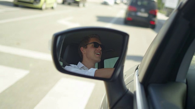 近距离观察:汽车侧镜中快乐男子驾车穿过城镇的画面。视频下载