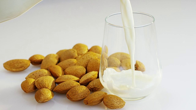 杏仁牛奶被慢镜头倒进玻璃杯里，背景是木头里有杏仁，完美的健康饮食和可以用作药物。视频素材
