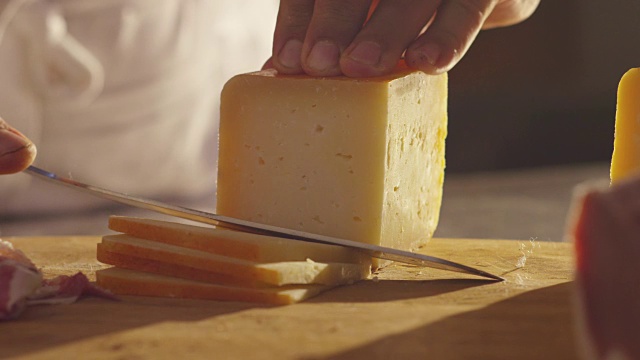 将意大利奶酪放在木砧板上。一只手拿着刀，掰开几块来品尝质量。视频下载